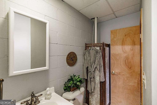 bathroom featuring toilet, concrete block wall, and a sink