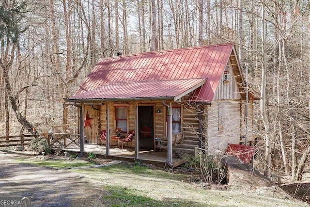 view of front of property featuring metal roof, an outbuilding, log exterior, and fence