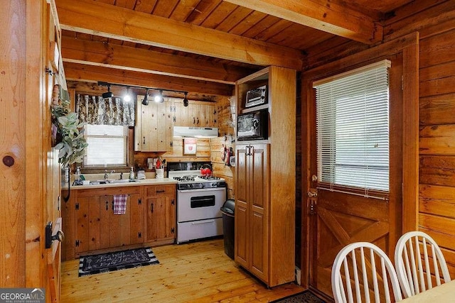 kitchen featuring range hood, beam ceiling, light wood-style flooring, gas range gas stove, and black microwave