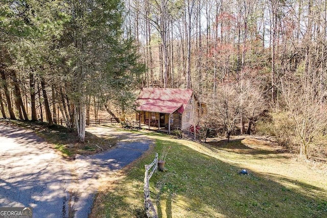 view of front of property featuring an outbuilding, fence, a forest view, a front lawn, and dirt driveway