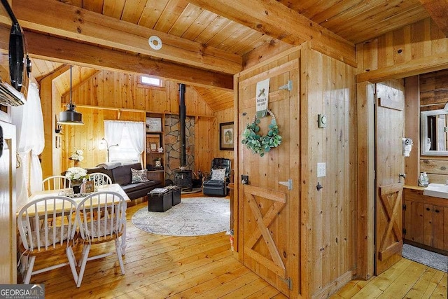 interior space with wooden ceiling, a wood stove, wooden walls, and light wood finished floors