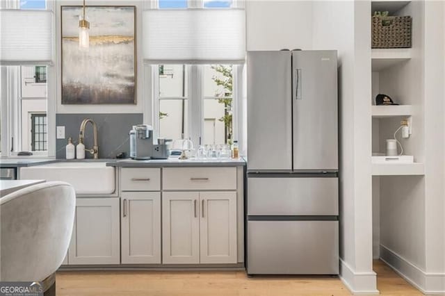 kitchen with built in shelves, baseboards, light wood-type flooring, freestanding refrigerator, and a sink