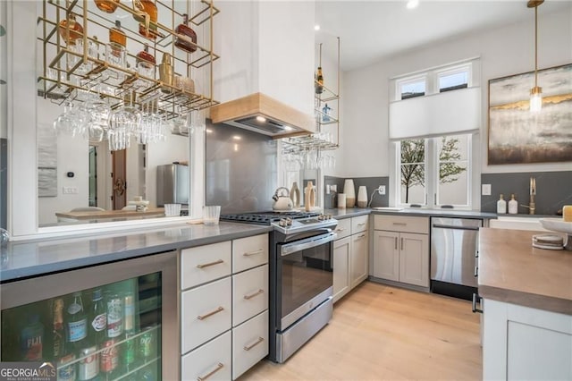 kitchen featuring light wood finished floors, wine cooler, backsplash, a high ceiling, and appliances with stainless steel finishes
