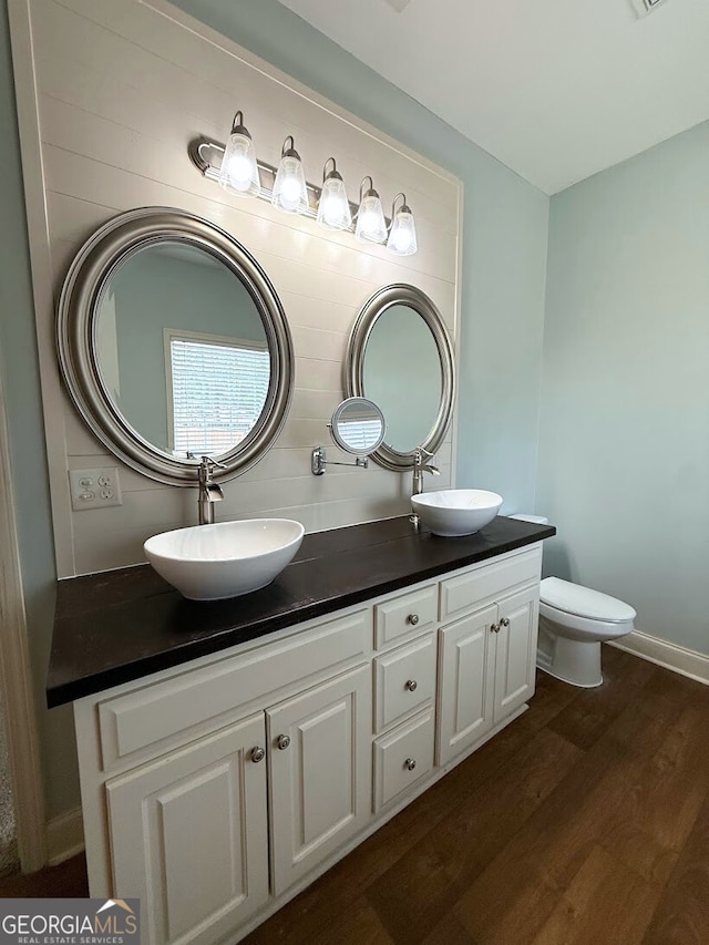 bathroom featuring a sink, toilet, wood finished floors, and double vanity