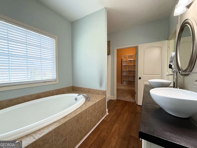 bathroom featuring a spacious closet, a sink, a garden tub, and wood finished floors