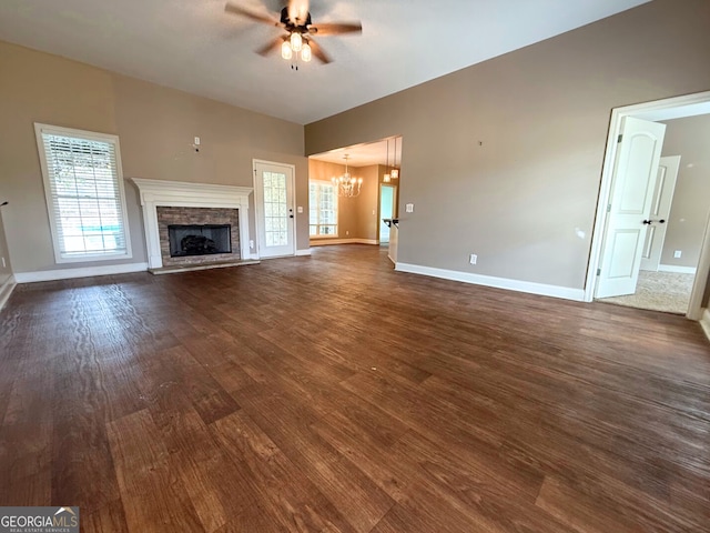 unfurnished living room with dark wood finished floors, ceiling fan with notable chandelier, a fireplace, and baseboards