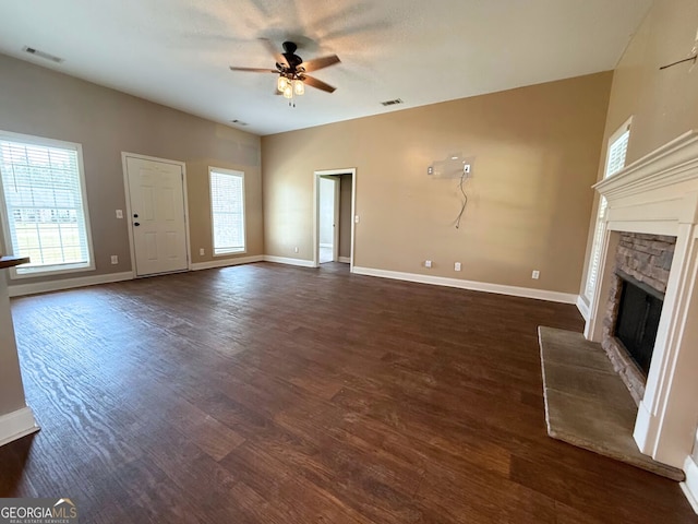 unfurnished living room with baseboards, visible vents, a fireplace, dark wood-style flooring, and ceiling fan