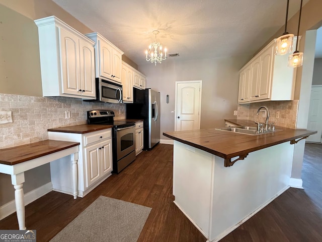 kitchen featuring visible vents, butcher block counters, a peninsula, stainless steel appliances, and a sink