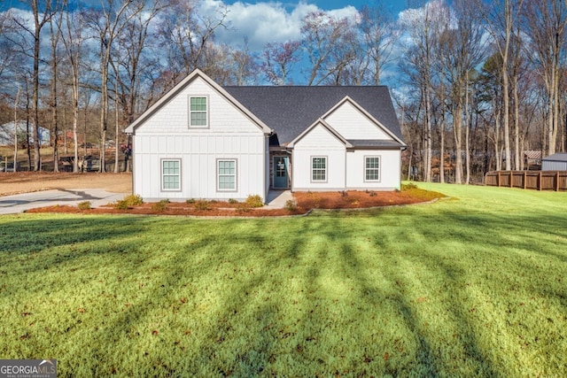 modern inspired farmhouse featuring roof with shingles, board and batten siding, a front yard, and fence