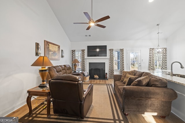 living room featuring high vaulted ceiling, wood finished floors, a fireplace, baseboards, and ceiling fan