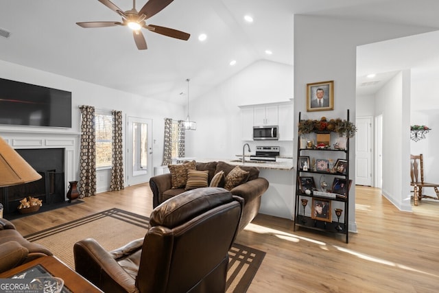 living room with a fireplace with flush hearth, light wood-style flooring, high vaulted ceiling, and ceiling fan with notable chandelier