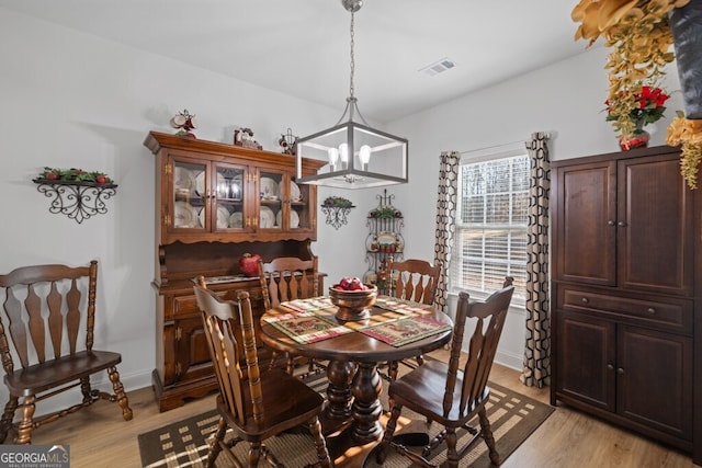 dining space featuring visible vents, light wood-style flooring, baseboards, and an inviting chandelier