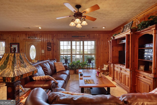 living area featuring a ceiling fan, a textured ceiling, light tile patterned flooring, and wooden walls