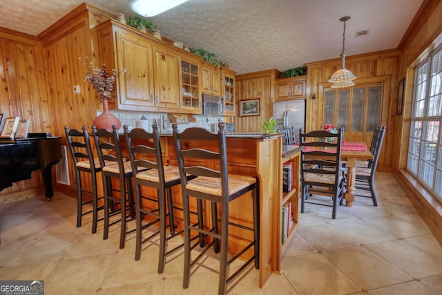 kitchen with visible vents, stainless steel appliances, glass insert cabinets, wood walls, and a textured ceiling