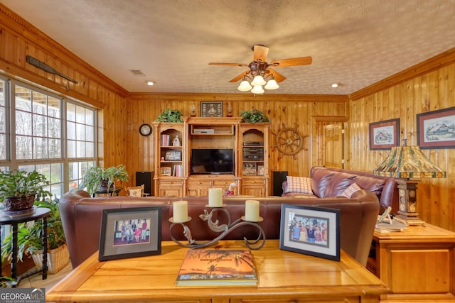 living area featuring wood walls, a textured ceiling, crown molding, and ceiling fan