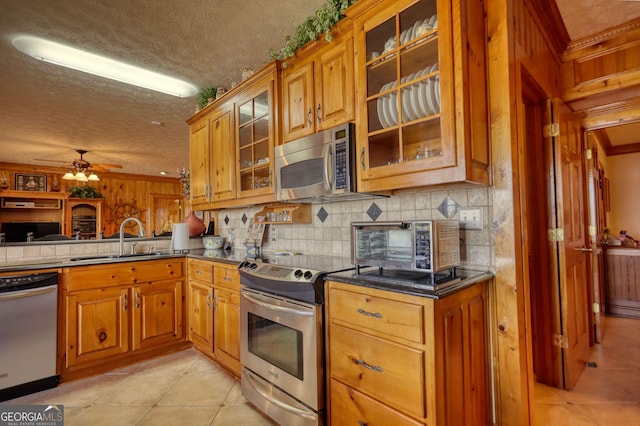 kitchen featuring a sink, backsplash, appliances with stainless steel finishes, light tile patterned flooring, and brown cabinetry