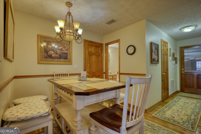 dining space featuring an inviting chandelier, wood finished floors, visible vents, and a textured ceiling