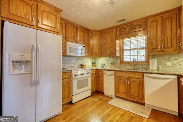 kitchen featuring light wood-type flooring, visible vents, white appliances, brown cabinetry, and light stone countertops