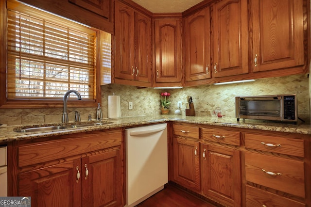 kitchen featuring brown cabinets, light stone counters, white dishwasher, and a sink