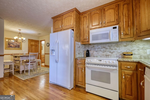 kitchen with a textured ceiling, tasteful backsplash, white appliances, light wood-style floors, and brown cabinetry