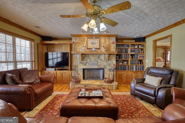 living room with visible vents, light wood-style flooring, ornamental molding, a textured ceiling, and a stone fireplace