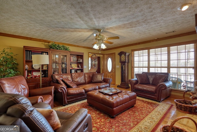 living room featuring a ceiling fan, wood finished floors, visible vents, ornamental molding, and a textured ceiling