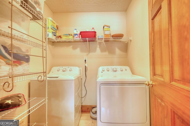 clothes washing area featuring washer and dryer, a textured ceiling, laundry area, and light tile patterned floors