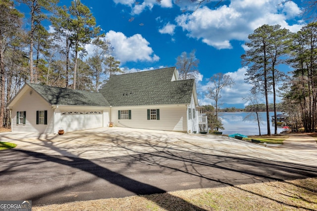 view of side of home featuring a garage, a water view, driveway, and a shingled roof