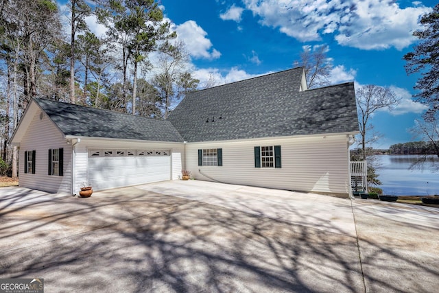 view of property exterior with concrete driveway, an attached garage, a water view, and roof with shingles