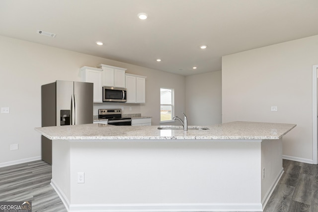 kitchen with wood finished floors, a sink, a large island, appliances with stainless steel finishes, and white cabinetry