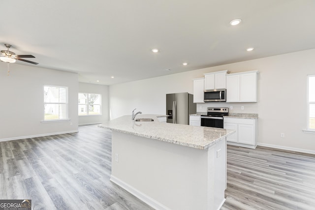 kitchen with light wood finished floors, a kitchen island with sink, white cabinets, stainless steel appliances, and a sink