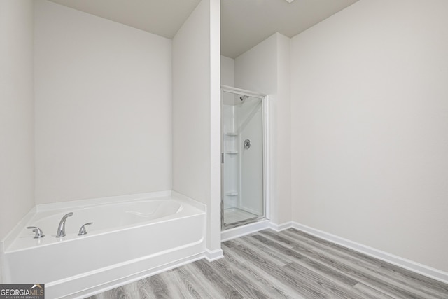 bathroom with a bath, a shower stall, baseboards, and wood finished floors