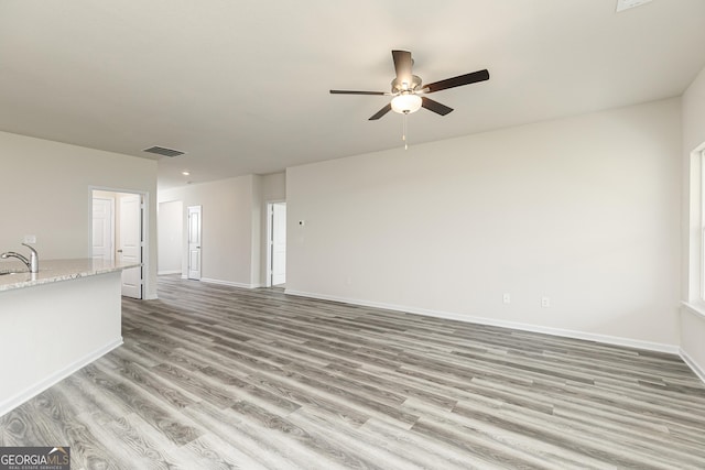 unfurnished living room featuring baseboards, visible vents, a sink, ceiling fan, and light wood-type flooring