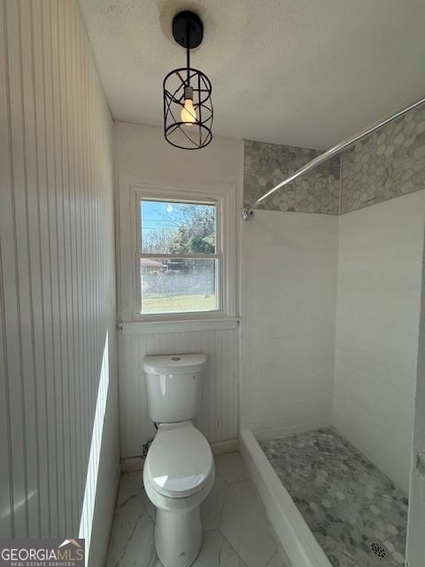 bathroom with marble finish floor, a stall shower, toilet, and a textured ceiling