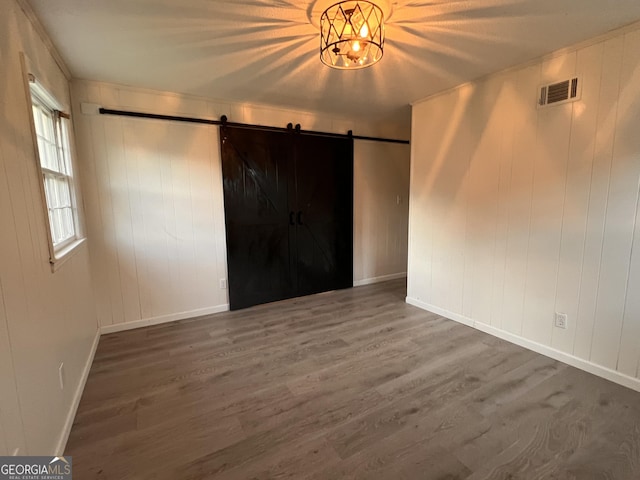 unfurnished room featuring a barn door, wood finished floors, visible vents, and baseboards