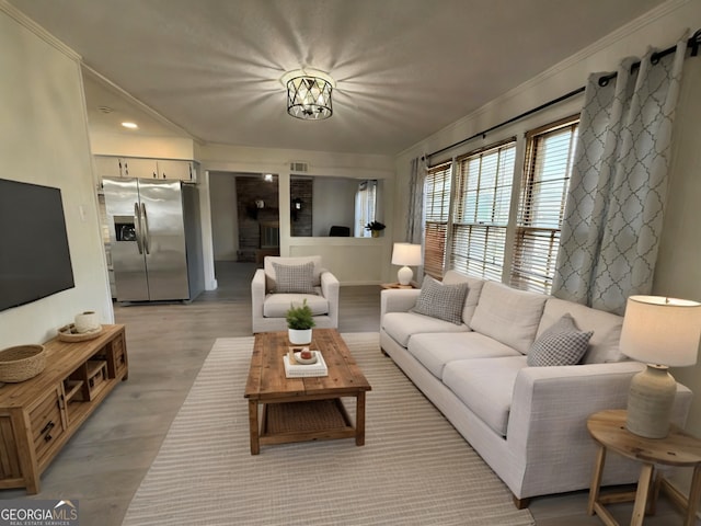 living area with a notable chandelier, light wood-style floors, visible vents, and ornamental molding