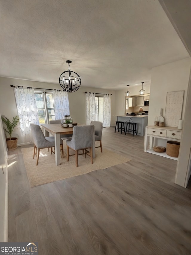 dining room featuring a textured ceiling, a healthy amount of sunlight, wood finished floors, and an inviting chandelier