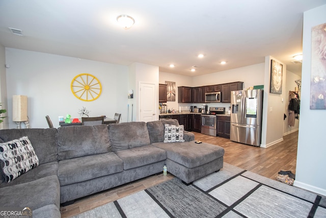 living area with recessed lighting, visible vents, light wood finished floors, and baseboards