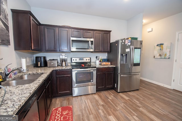 kitchen featuring a sink, light stone counters, stainless steel appliances, light wood finished floors, and dark brown cabinets