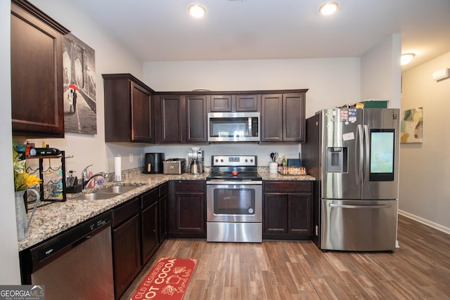 kitchen with dark brown cabinetry, wood finished floors, appliances with stainless steel finishes, and a sink