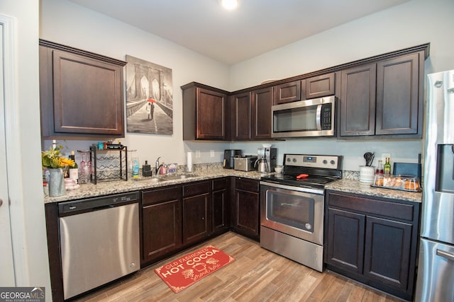 kitchen featuring dark brown cabinets, light stone countertops, appliances with stainless steel finishes, and light wood finished floors