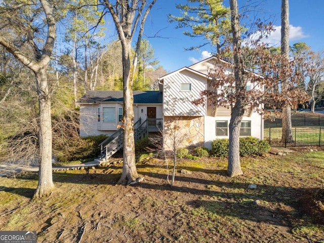 view of front of home with stone siding, stairway, and fence