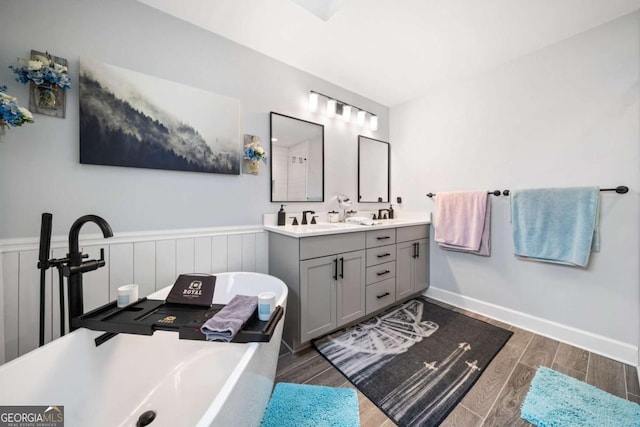 bathroom featuring wood finish floors, a freestanding tub, a wainscoted wall, a sink, and double vanity