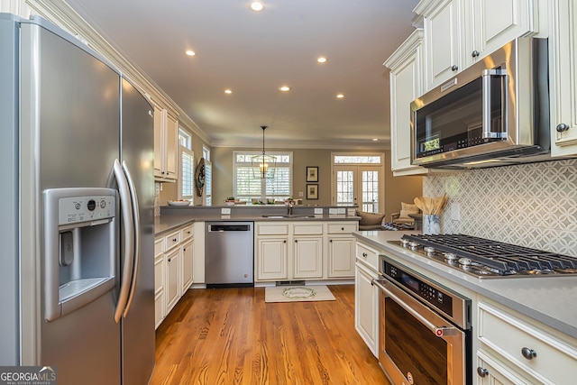 kitchen with light wood-style flooring, ornamental molding, stainless steel appliances, a peninsula, and decorative backsplash