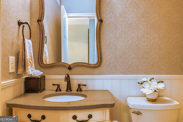 bathroom featuring vanity, toilet, and a wainscoted wall