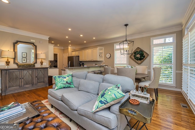 living area with visible vents, wood finished floors, ornamental molding, and a chandelier