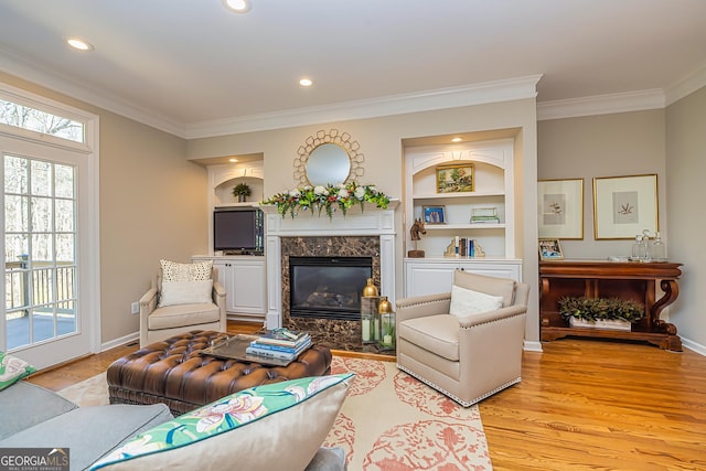 living area featuring light wood-type flooring, built in shelves, ornamental molding, a fireplace, and baseboards