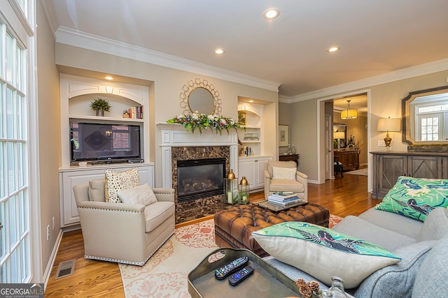 living room with built in shelves, wood finished floors, visible vents, and ornamental molding