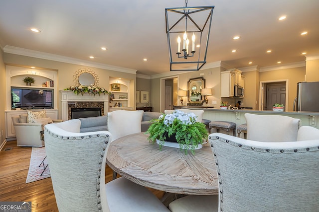 dining space featuring built in shelves, light wood-style flooring, recessed lighting, crown molding, and a premium fireplace