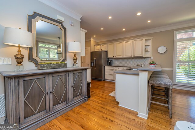 kitchen featuring open shelves, a peninsula, light wood-style floors, stainless steel refrigerator with ice dispenser, and a sink